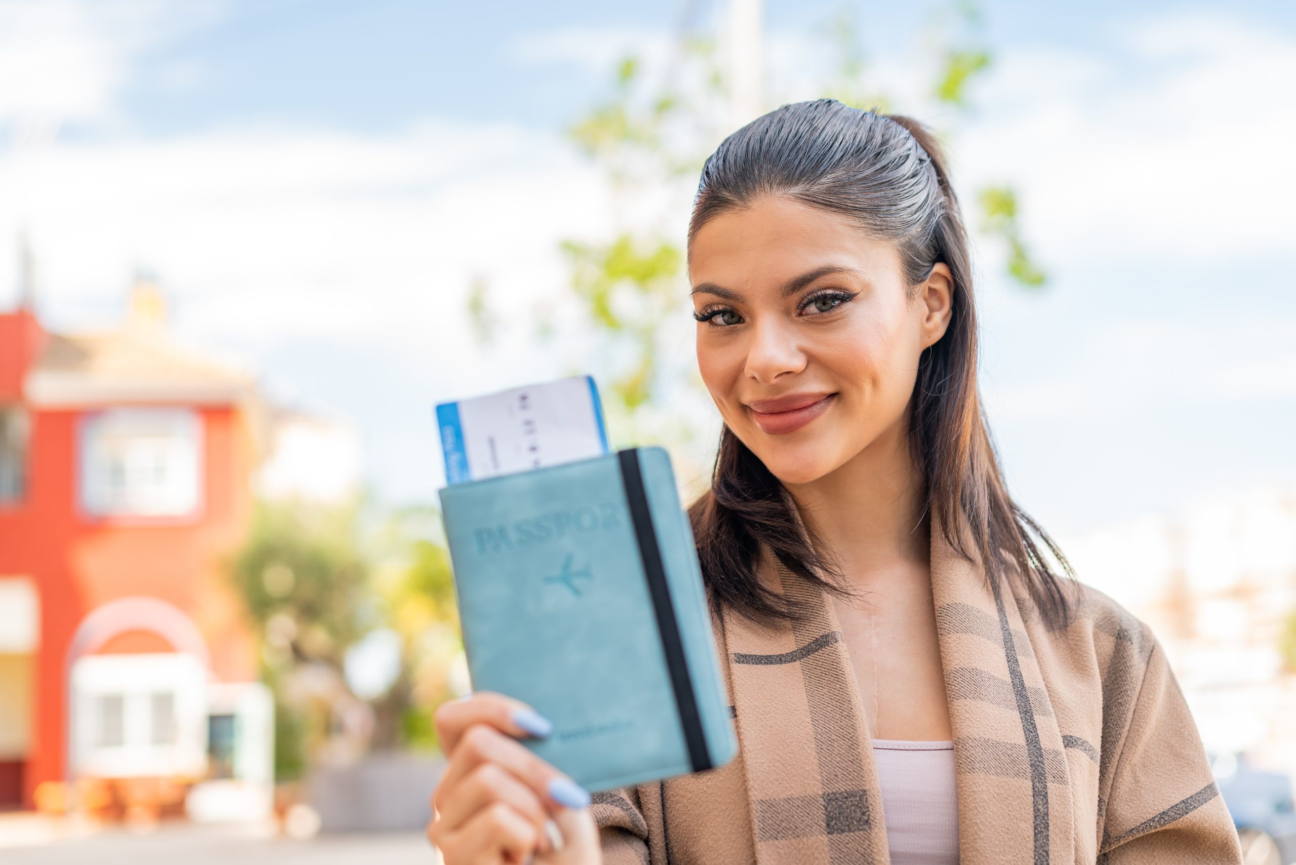 Young pretty woman holding a passport at outdoors with happy expression